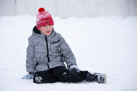 The boy sits in the snow in winter.