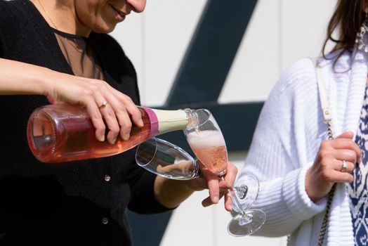 closeup of a champagne bottle pooring pink champagne into a champagne flute against a blurred person at a party