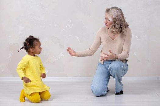 Multiethnic mom and daughter play at home. Cheerful mother with little daughter of African nationality. Family from different races.