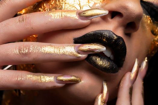 Beauty fashion model girl with golden make-up and body on black background. Golden body art. The golden face of a beautiful lady is touching. Artistic portrait.