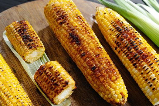 A cob of corn roasted over charcoal on a wooden board. Whole corn cobs. Close up