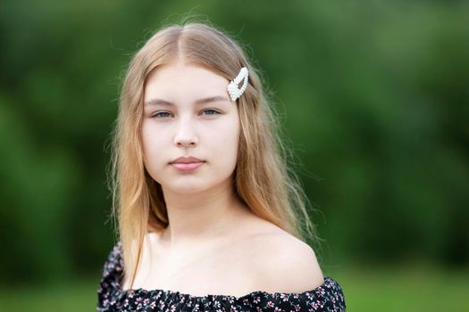 Portrait of a beautiful girl with long hair on a summer background. The face of a fair-haired teenage girl.