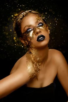 Fashion art Golden skin. Girl Model with Festive Golden Glamor Brilliant Professional Makeup. Creative makeup with golden foil.