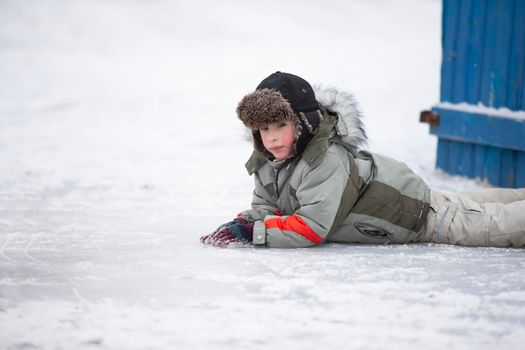 A little boy in a fur hat lies on the snow. Child in winter.