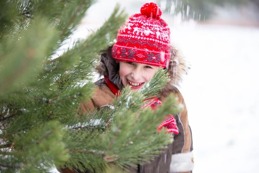 Funny little boy among the snow-covered Christmas trees. Child in winter.