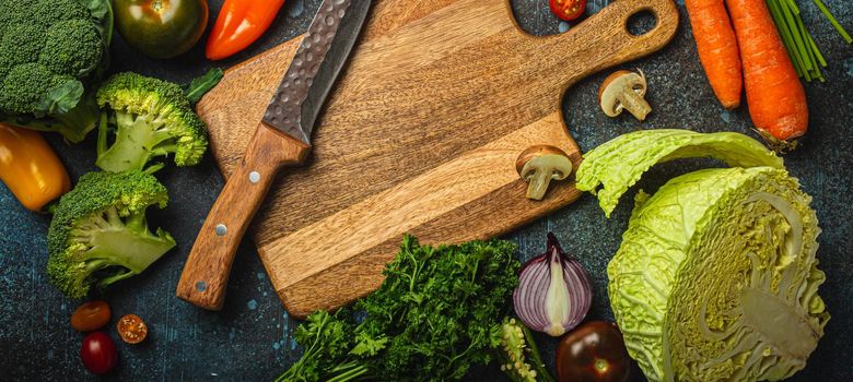 Assorted fresh vegetables on rustic concrete table with wooden cutting board in center and kitchen knife, diet and vegetarian food preparing and meal cooking concept, healthy lifestyle