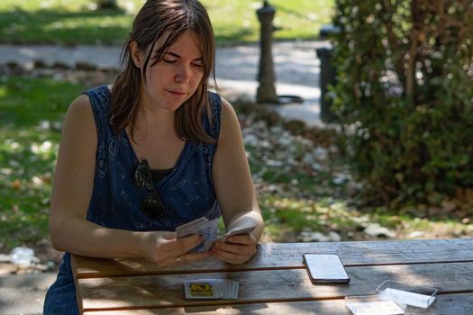 young woman playing cards in the park on a sunny day wearing a blue dress