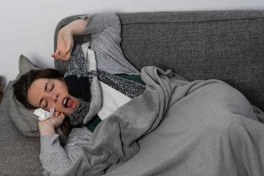 young brunette girl with long hair, sick lying on the sofa in her house taking medicine and an infusion