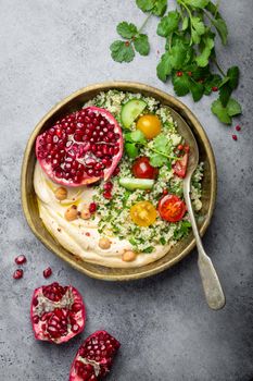 Rustic bowl with couscous salad with vegetables, hummus and fresh cut pomegranate. Middle eastern or Arab style meal with seasonings and fresh cilantro. Beautiful and healthy Mediterranean dinner .