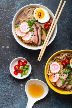 Cooking Japanese noodle soup ramen. Ramen with sliced pork, narutomaki, egg and kitchen spoon with broth on rustic stone background. Making traditional dish of Japan, top view, close-up, concept