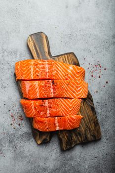 Top view, close-up of cut in slices fresh raw salmon fillet with seasonings on wooden board, gray stone background. Preparing salmon fillet for cooking, healthy eating concept