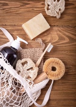 Fishnet shopping bag with ethical eco-friendly cleaning household products: sisal brush, natural luffa, bamboo toothbrush, organic soap in bottle, wooden pins. Conscious consumption concept.