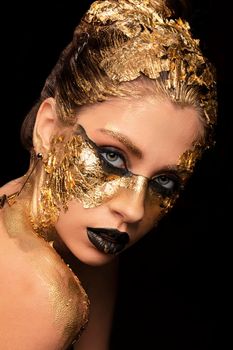 Closeup portrait of beautiful young woman with golden foil on face. Creative golden makeup on black background