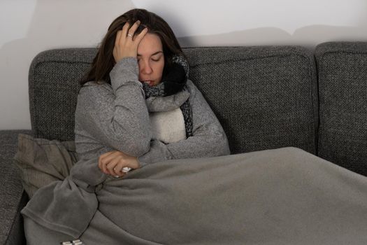 young brunette girl with long hair, sick lying on the sofa in her house taking medicine and an infusion