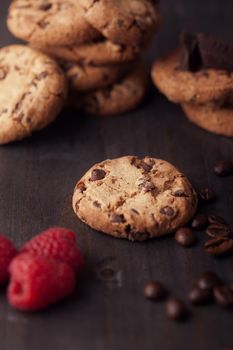 Chocolate chips cookies with red raspberries and coffee beans on dark old wooden table. Fresh out of the oven.