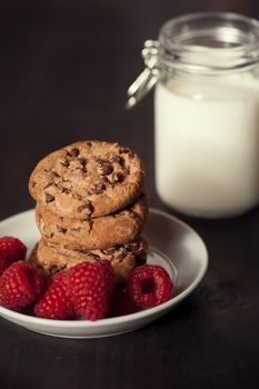 Chocolate chip cookies with red raspberry and milk on rustic wood background. Homemade dessert.