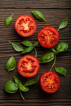 Cooking food ingredients background concept, pattern. Cut fresh red tomato and green basil leaves on wooden rustic background, closeup, top view