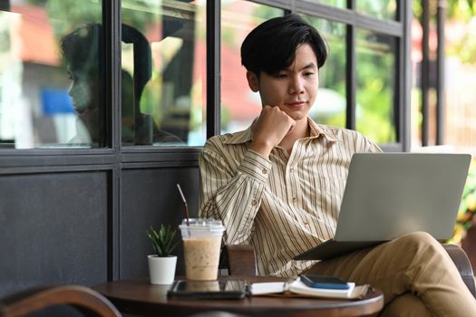 Handsome Asian man sitting outdoor cafe and working with laptop computer.
