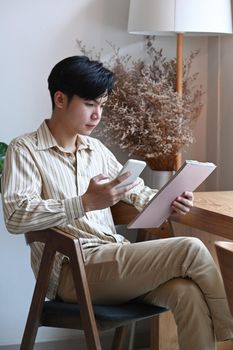 Handsome Asian man holding smart phone and using digital tablet in cafe.