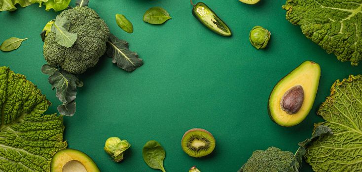 Creative layout food concept made of green fruit and vegetables on green background flat lay: avocado, kale, broccoli, Brussels sprouts, kiwi, peppers, apple, cabbage top view with space for text.