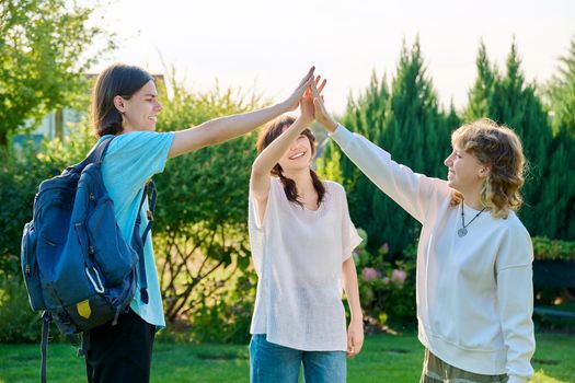 Meeting of three teenage friends, outdoor on a sunny day. Teenagers 17, 18 years old greeting, cheering, rejoicing, communication friendship lifestyle youth concept