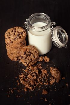 Homemade chocolate chip cookies with bottle of milk and crumbs on rustic wooden table.
