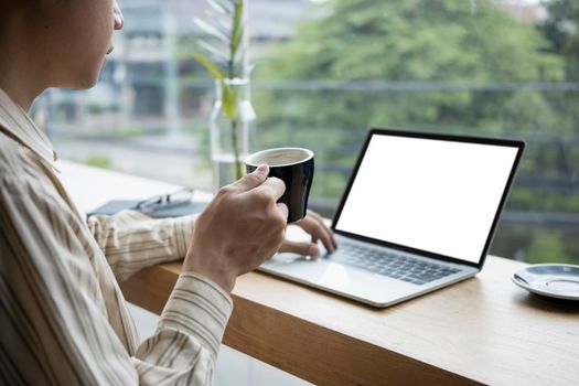 Cropped shot businessman holding coffee cup and working with laptop computer.