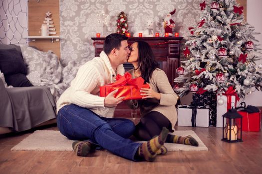 Beautiful young couple kissing near a christmas tree in a cozy home. Christmas decoration,