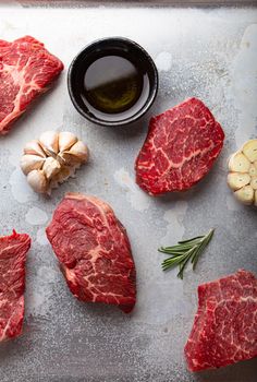 Raw uncooked meat beef cubes for stew or roasting with seasonings, olive oil, garlic and fresh rosemary on rustic aluminum baking tray from above