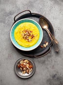 Traditional Indian dish Kheer, sweet rice milk pudding with almonds and saffron in blue ceramic bowl with spoons on stone rustic background, top view. Dessert meal of Indian cuisine