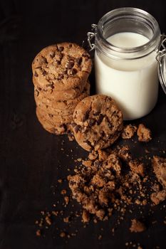 Homemade chocolate chip cookies with bottle of milk and crumbs on rustic wooden table. Sweet dessert.