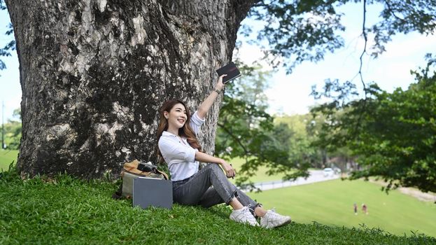 Cheerful woman sitting on the green grass and breathing fresh air in the park. Healthcare lifestyle and wellness.