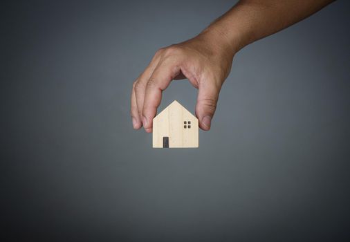 Concept of selling a house. A hand is holding a model house on a gray background. Real estate agent offer house, property insurance and security, affordable housing concepts, home insurance broker agent, salesman person.