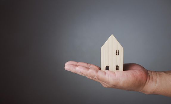 Concept of selling a house. A hand is holding a model house on a gray background. Real estate agent offer house, property insurance and security, affordable housing concepts, home insurance broker agent, salesman person.