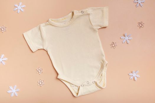Yellow baby bodysuit mockup for logo, text or design on pink background with winter decotations top view