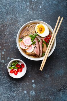 Tasty Japanese noodle soup ramen in white ceramic bowl with meat broth, sliced pork, narutomaki, egg with yolk on rustic stone background. Traditional dish of Japan, top view, close-up, concept