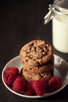 Chocolate chip cookies with red raspberry and milk on rustic wood background. Homemade dessert.