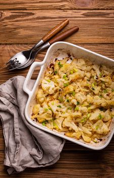 Baked cauliflower with herbs in white ceramic tray on rustic wooden background table, top view. Vegetarian healthy food, clean eating concept .