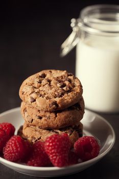 Chocolate chip cookies with red raspberry and milk on rustic wood background. Homemade dessert.