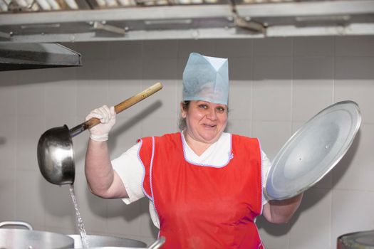 A woman cook in an industrial kitchen with a large ladle among metal pans. Chef at the hospital