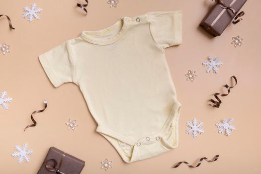 Yellow baby bodysuit mockup for logo, text or design on beige background with winter decotations top view.