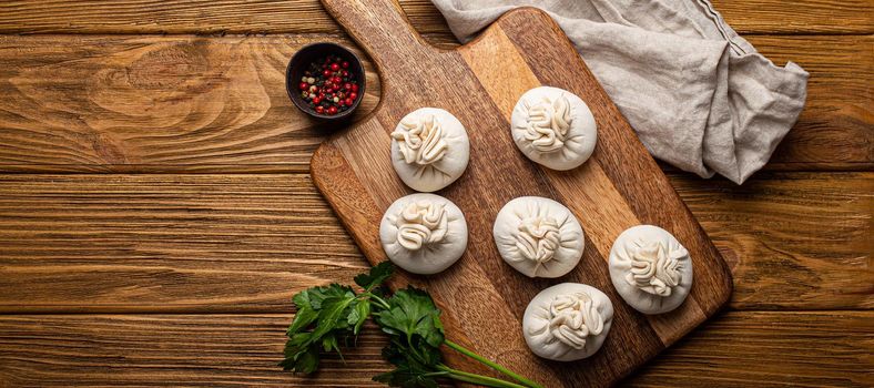 Raw freshly made Khinkali, traditional dish of Georgian Caucasian cuisine, dumplings filled with ground meat on white plate with herbs on wooden rustic background table top view space for text.
