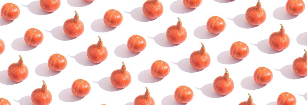 Pattern made from orange pumpkins with hard shadows on white background. Banner format.