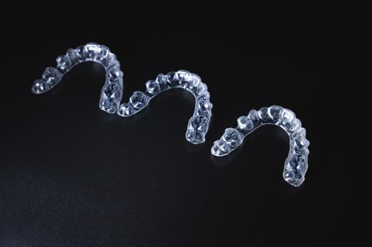 three invisible plastic aligners lie next to each other on a black background.