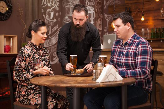 Hipster barman giving the order to beautiful young couple.Great Pub.