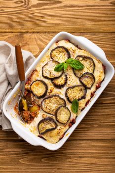 Greek mediterranean dish Moussaka with baked eggplants, ground beef in white ceramic casserole with napkin on wooden rustic background from above, traditional dish of Greece