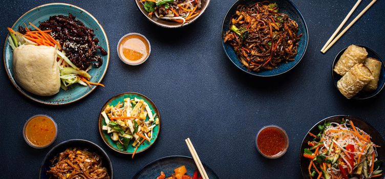 Set of Chinese dishes on table: sweet and sour chicken, fried spring rolls, noodles, rice, steamed buns with bbq glazed pork, Asian style banquet or buffet, top view with copy space.