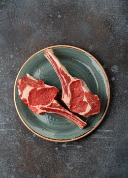 Two raw marbled Tomahawk meat steaks on plate, concrete background. Premium Beef steak on bone preparation, top view, steak house restaurant or butchery concept .
