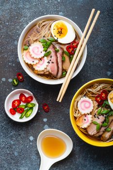 Cooking Japanese noodle soup ramen. Ramen with sliced pork, narutomaki, egg and kitchen spoon with broth on rustic stone background. Making traditional dish of Japan, top view, close-up, concept