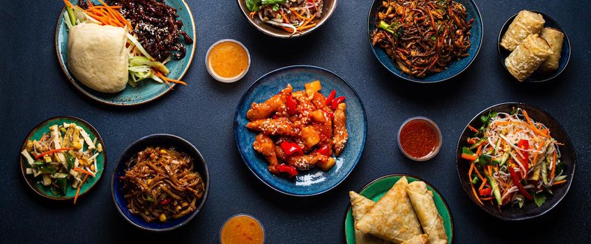 Set of assorted Chinese dishes on table: sweet and sour chicken on plate, fried spring rolls, noodles, salad, rice, steamed buns with bbq glazed pork, Asian style banquet or buffet, top view .